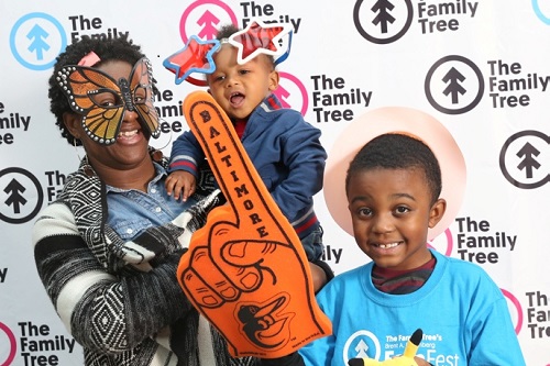 smiling adult and two children with silly masks and foam finger