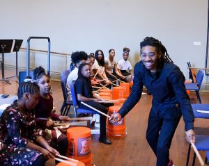 smiling teacher instructing students drumming on buckets