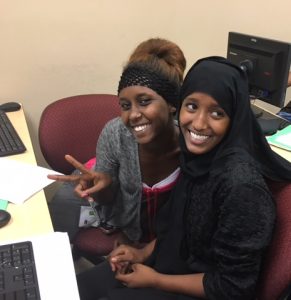 young women at computer smile at camera